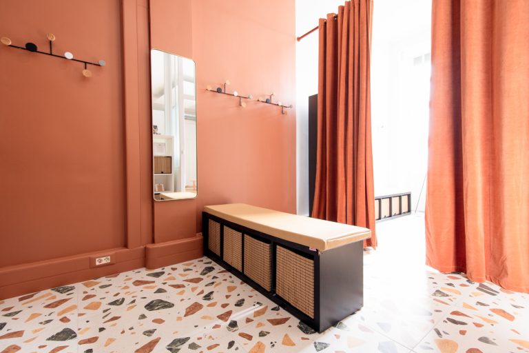 Intérieur moderne avec murs orange, banc en bois et rideaux rouges, sol en terrazzo.