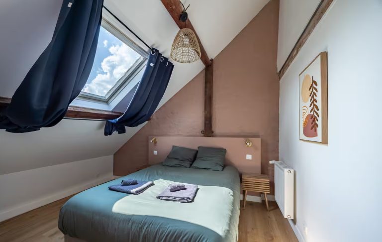 Chambre mansardée avec lit double, murs en brique rouge et fenêtres lumineuses.