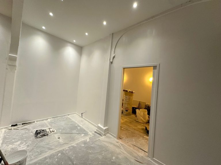 Intérieur d'une pièce en cours de rénovation, murs peints en blanc, sol en désordre.