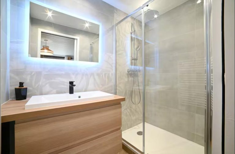 Salle de bains moderne avec douche vitrée et meuble en bois clair.