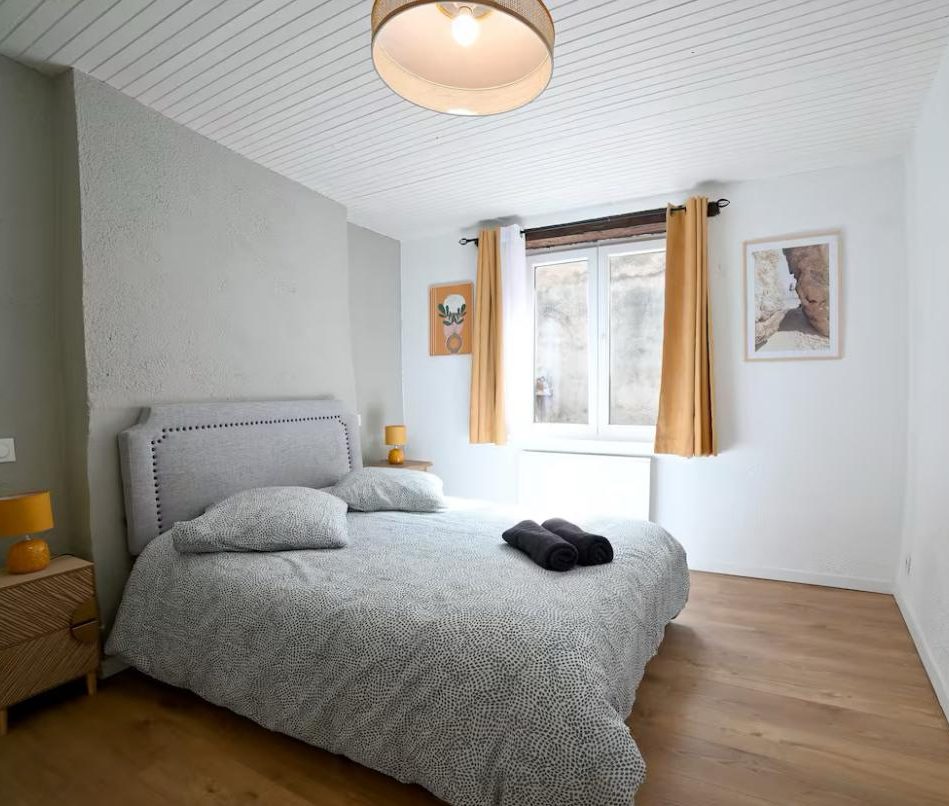 Chambre lumineuse avec un lit double, des coussins et des rideaux jaunes.