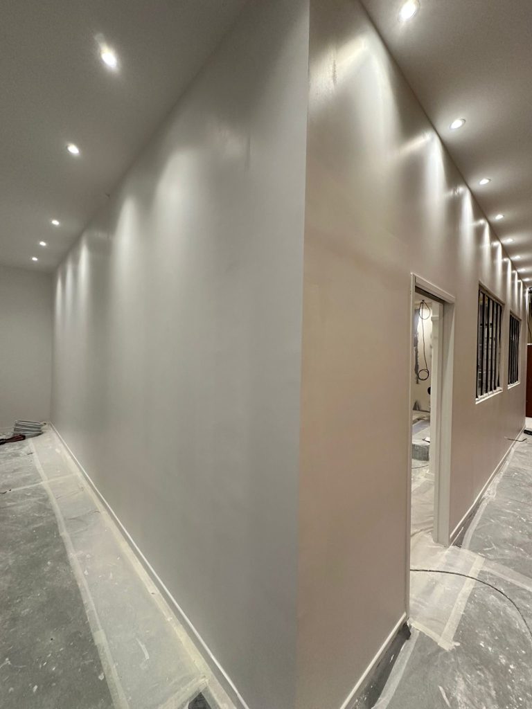 Mur intérieur fraîchement peint en gris, avec éclairage encastré au plafond.
