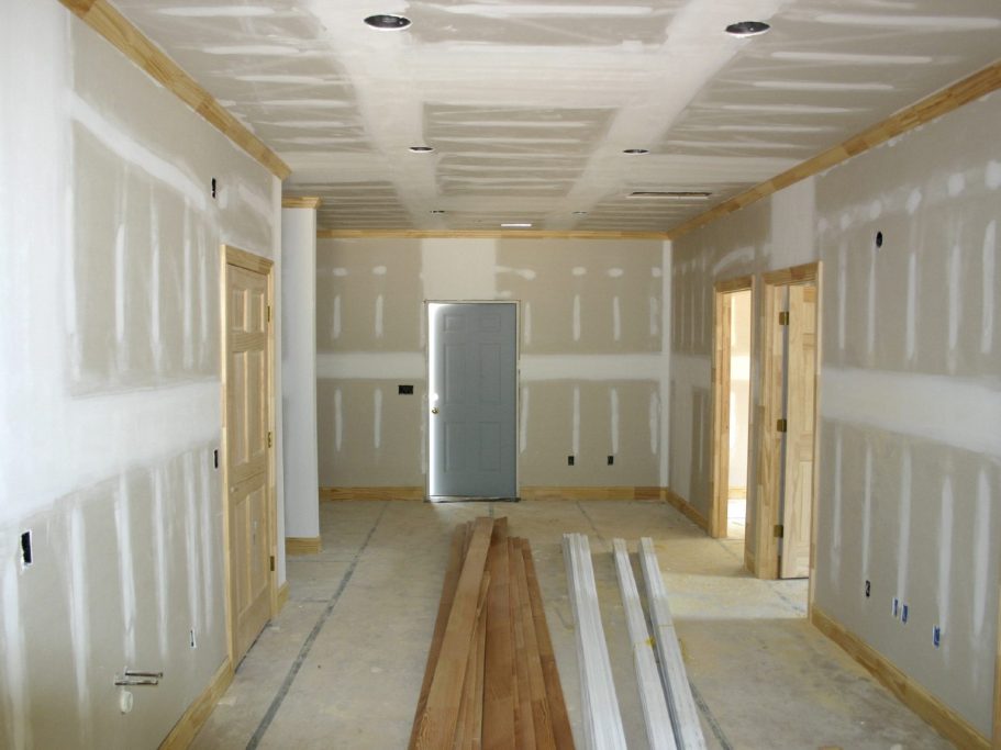 Intérieur d'une pièce en cours de finition, murs en plaques de plâtre et sol en bois.
