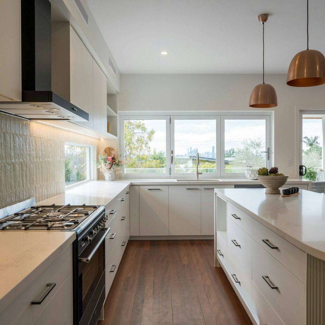 Cocina moderna con encimeras de mármol, electrodomésticos y ventanas luminosas.