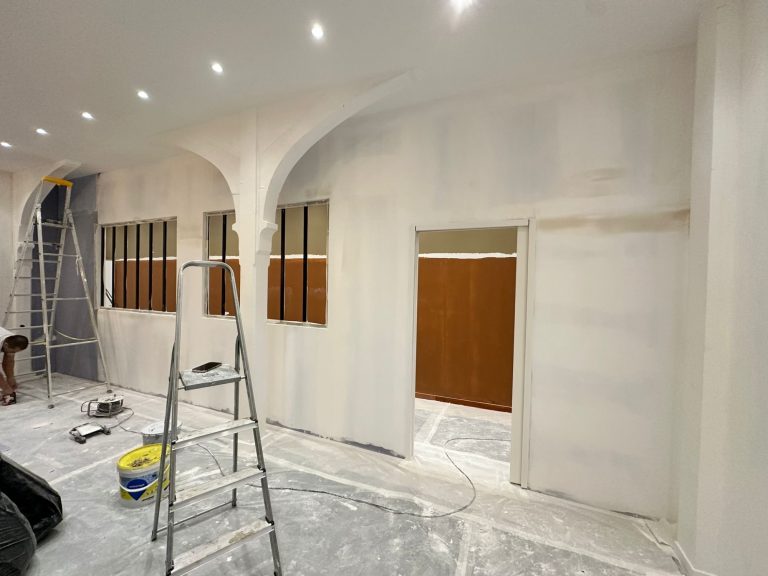 Mur en cours de peinture avec des zones blanches et un échafaudage à proximité.