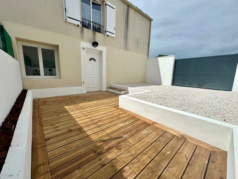 Terrasse en bois près d'une maison avec un mur blanc et une vue sur la mer.