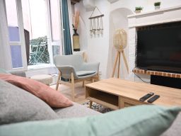 Salon lumineux avec canapé, table basse en bois, et téléviseur sur un mur blanc.