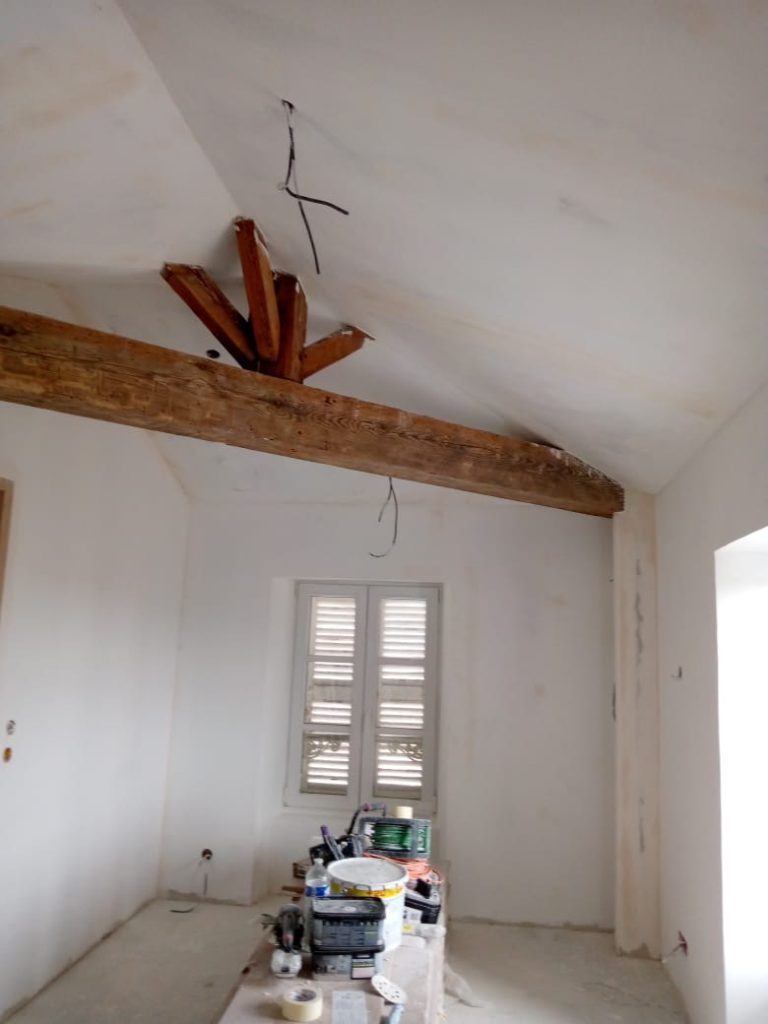 Salle vide avec des murs clairs, poutres apparentes et une table de travail au centre.