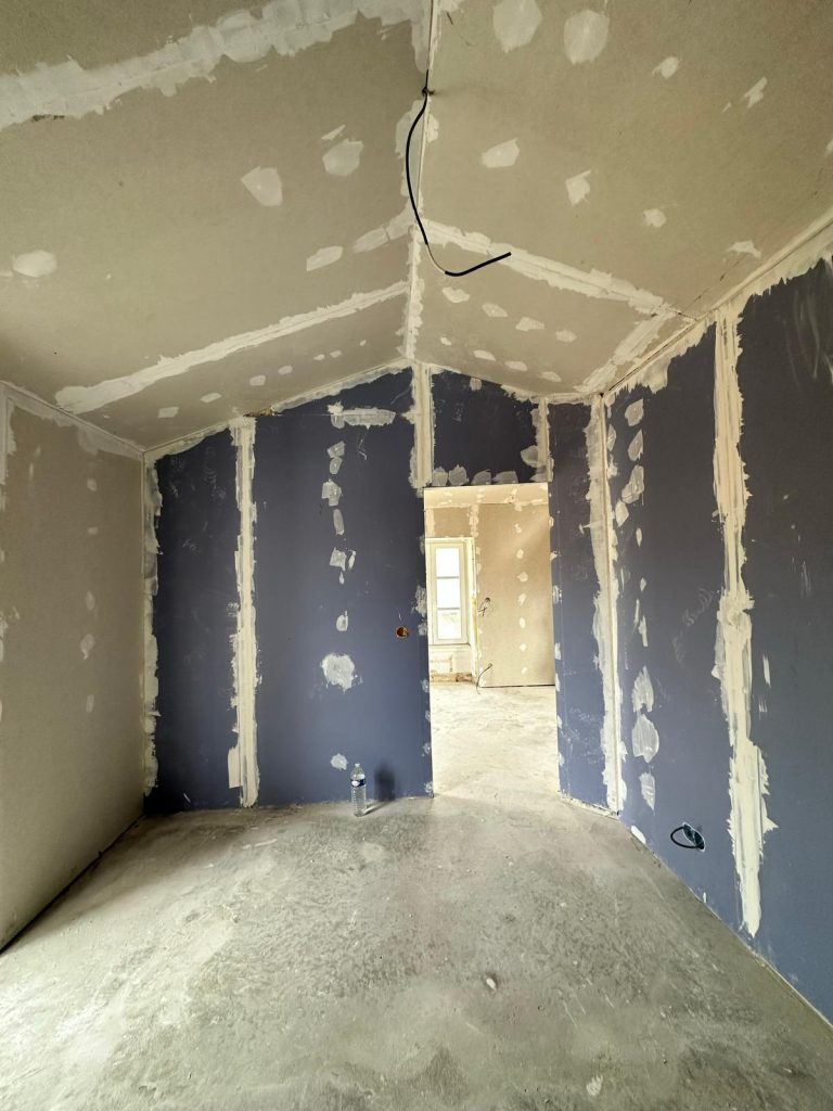 Salle en cours de rénovation avec murs en plâtre et sol en béton.