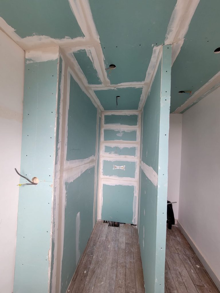 Couloir en cours de construction avec murs en plaques de plâtre et sol en bois.