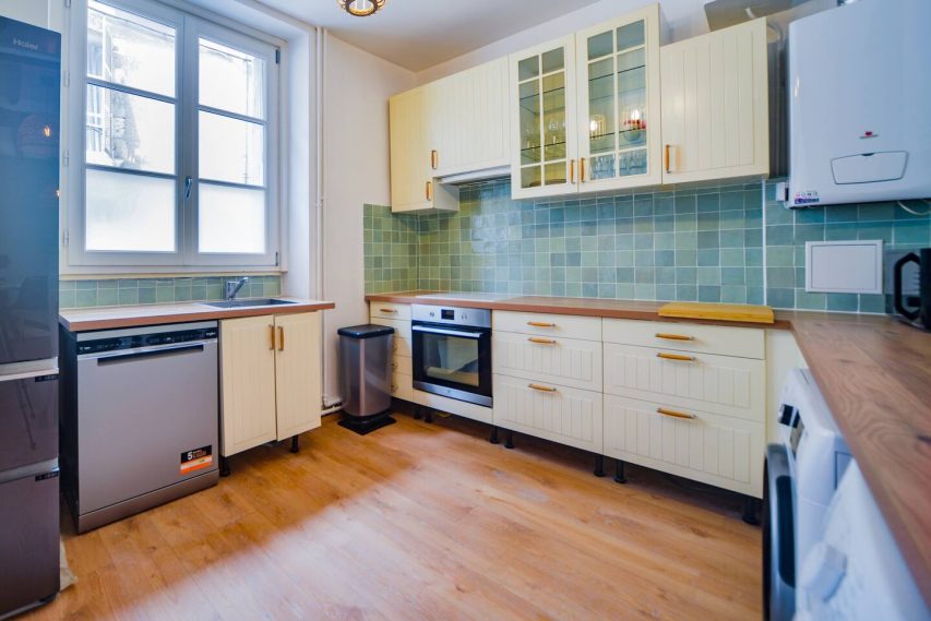 Cuisine lumineuse avec des meubles jaunes et des carrelages verts. Électroménagers en acier inoxydable.