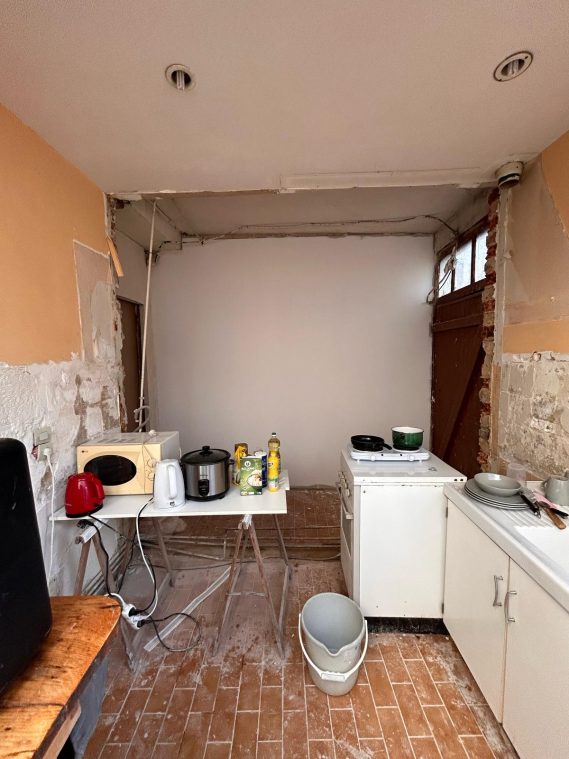 Cuisine en cours de rénovation, avec meubles et appareil électroménager sur un sol en mosaïque.