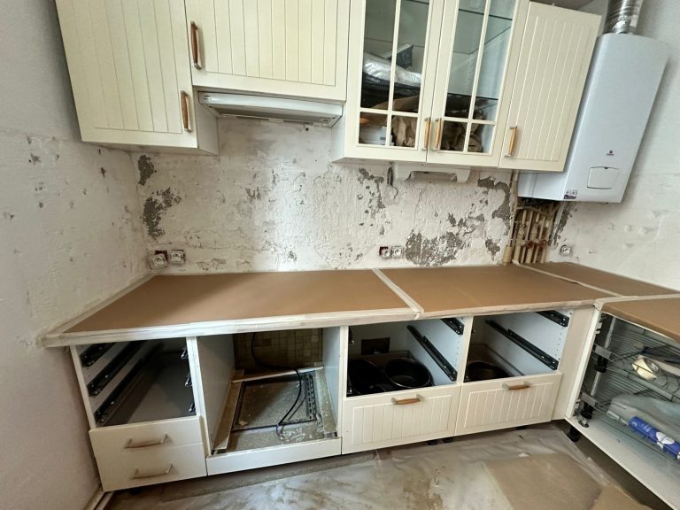 Cuisine en cours de rénovation avec des placards vides et un mur abîmé.