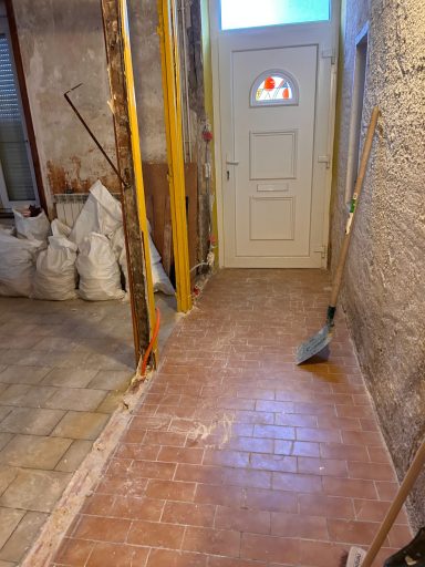 Couloir en rénovation avec des sacs, des outils et une porte blanche au fond.