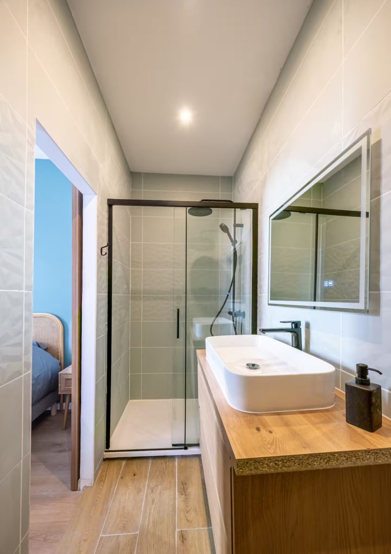 Salle de bain moderne avec douche en verre, lavabo sur meuble en bois et miroir.