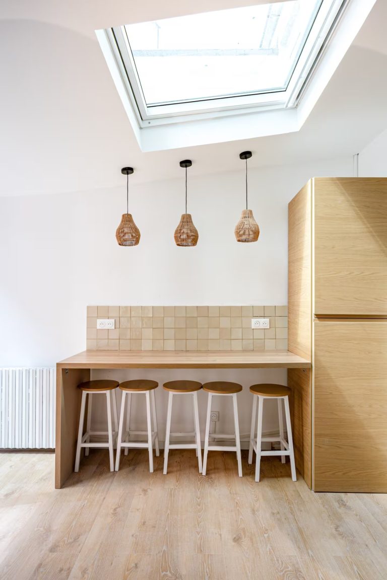 Cuisine moderne avec un comptoir en bois et trois tabourets sous des lampes suspendues.