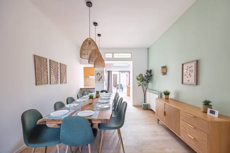 Salle à manger lumineuse avec table en bois, chaises vertes et murs verts clairs.