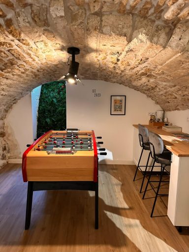 Salle de jeux avec une table de baby-foot et un bar sous une voûte en pierre.