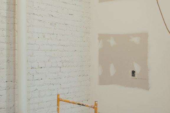 Pared de ladrillo blanco con secciones sin terminar y andamios de madera.